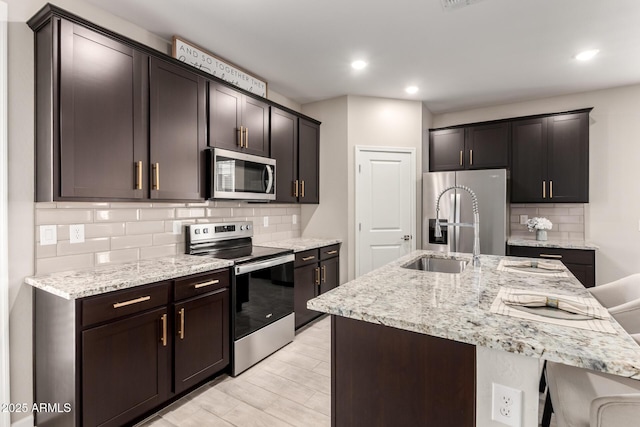 17437 W Via De Luna Dr, Surprise, AZ 85387 - kitchen featuring light stone countertops, appliances with stainless steel finishes, a sink, a kitchen breakfast bar, and tasteful backsplash
