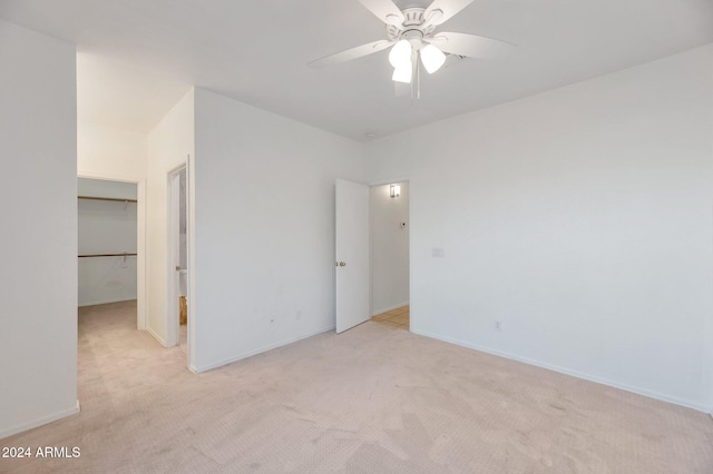 unfurnished bedroom with a walk in closet, a closet, light colored carpet, and ceiling fan