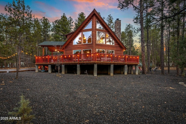 rear view of property featuring a wooden deck, faux log siding, and a chimney