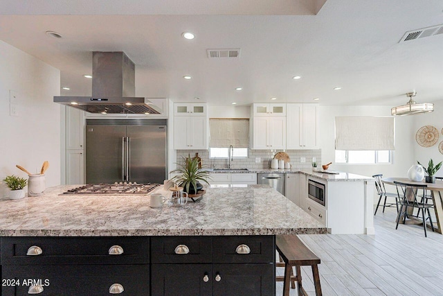 kitchen with white cabinets, island exhaust hood, built in appliances, sink, and a large island