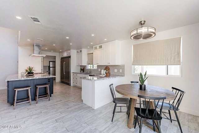 kitchen featuring light stone counters, high quality fridge, white cabinets, and extractor fan