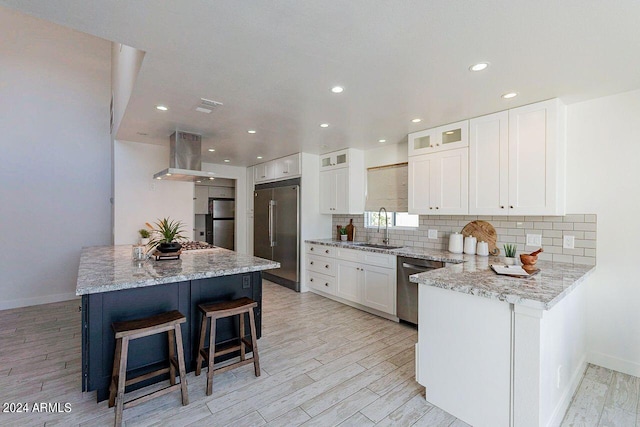 kitchen featuring appliances with stainless steel finishes, sink, white cabinetry, island exhaust hood, and light stone counters