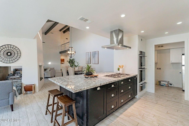 kitchen featuring a kitchen bar, stainless steel appliances, hanging light fixtures, island range hood, and light hardwood / wood-style flooring