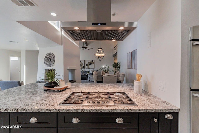 kitchen with ceiling fan with notable chandelier, light stone countertops, stainless steel gas stovetop, and range hood