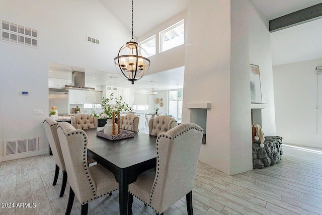 dining space with beam ceiling, high vaulted ceiling, an inviting chandelier, and light hardwood / wood-style floors