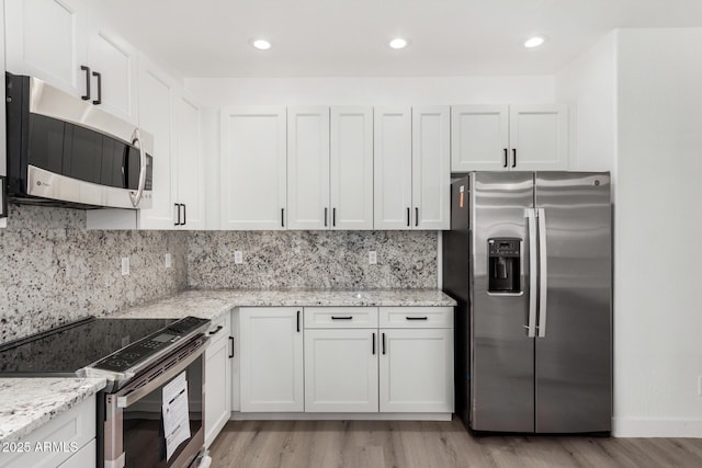 kitchen with white cabinets, decorative backsplash, light stone counters, stainless steel appliances, and light wood-type flooring