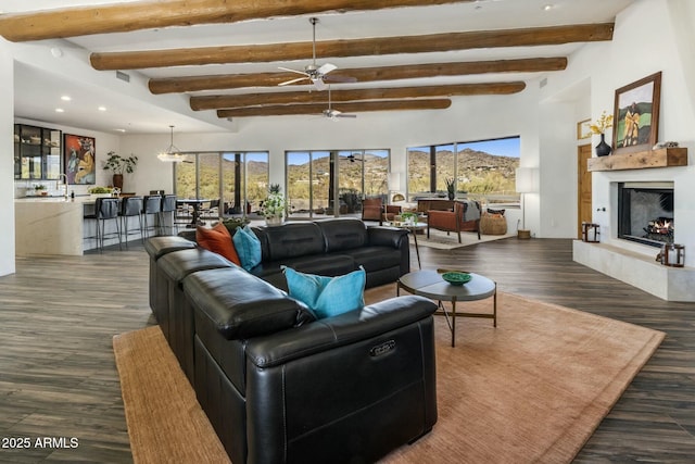 living room with recessed lighting, wood finished floors, a ceiling fan, a lit fireplace, and beam ceiling