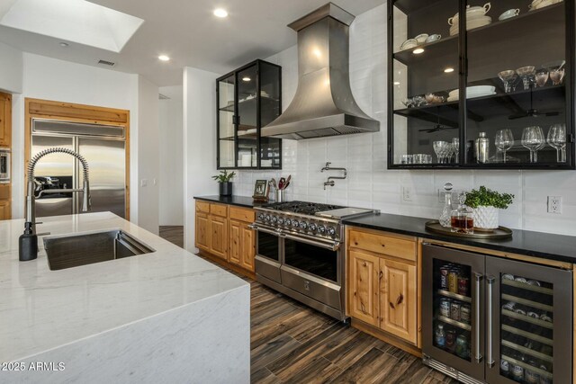 kitchen with premium appliances, dark wood-style floors, a sink, beverage cooler, and wall chimney exhaust hood