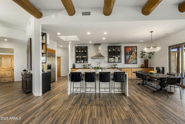 kitchen featuring visible vents, light countertops, decorative backsplash, wall chimney exhaust hood, and stainless steel built in refrigerator