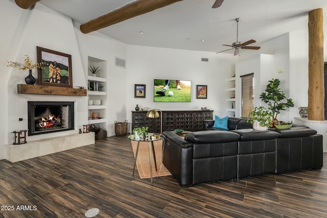 living room featuring built in shelves, beam ceiling, a fireplace, and wood finished floors