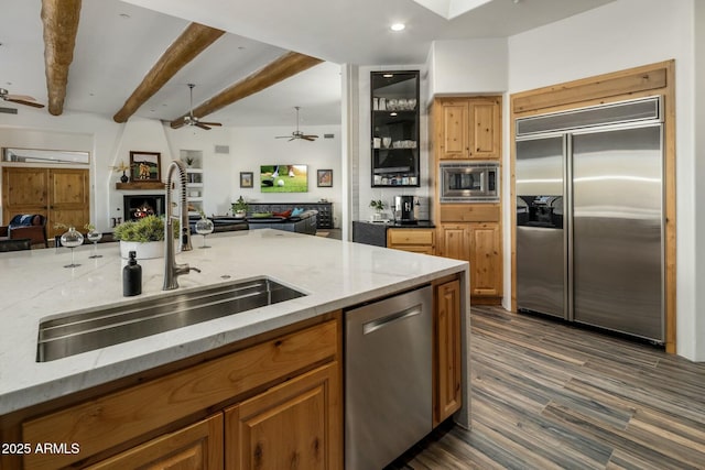 kitchen with built in appliances, a large fireplace, a sink, open floor plan, and light stone countertops