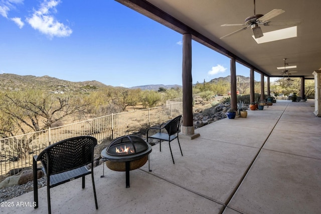 view of patio / terrace with ceiling fan, an outdoor fire pit, fence, and a mountain view