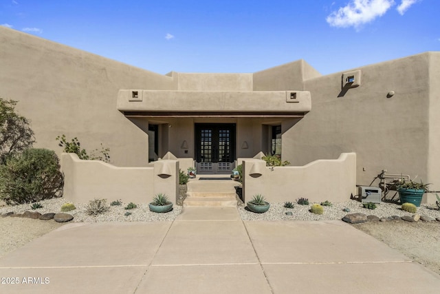 entrance to property with stucco siding, covered porch, and french doors