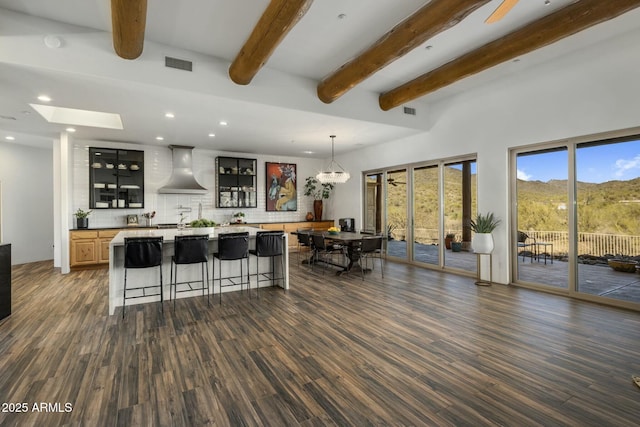 kitchen featuring visible vents, a kitchen breakfast bar, dark wood-style floors, wall chimney exhaust hood, and glass insert cabinets