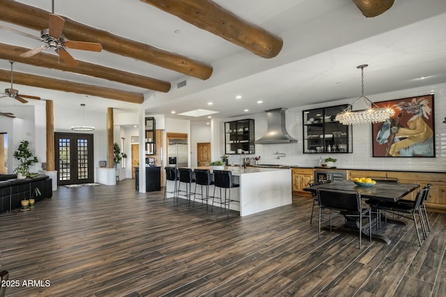 kitchen featuring dark wood finished floors, wall chimney exhaust hood, glass insert cabinets, french doors, and a kitchen bar