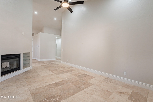 unfurnished living room with built in shelves, ceiling fan, and a towering ceiling