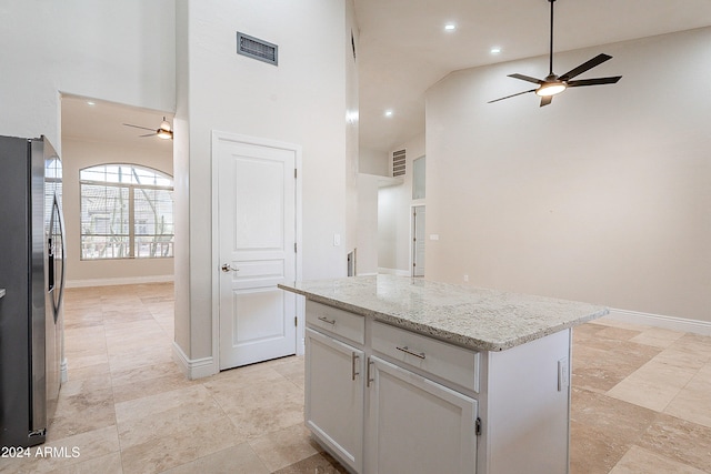 kitchen featuring high vaulted ceiling, stainless steel fridge, light stone countertops, a kitchen island, and white cabinetry