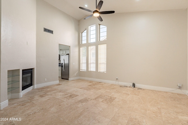 unfurnished living room featuring ceiling fan and a towering ceiling