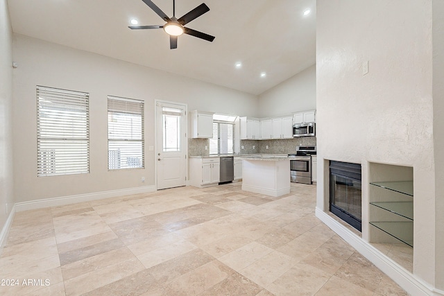 kitchen with stainless steel appliances, a kitchen island, ceiling fan, high vaulted ceiling, and white cabinetry