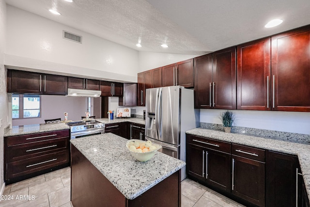 kitchen with vaulted ceiling, a textured ceiling, light tile floors, a center island, and appliances with stainless steel finishes