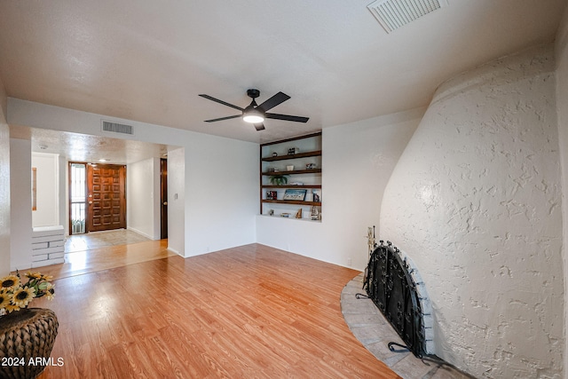 living room featuring ceiling fan, built in shelves, and light wood-type flooring