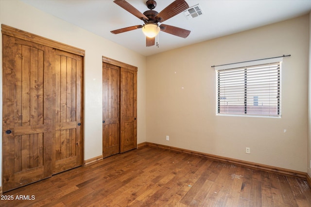 unfurnished bedroom with multiple closets, visible vents, baseboards, and wood finished floors