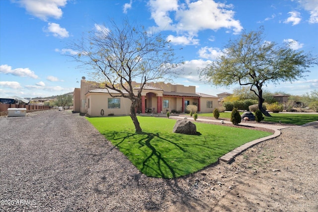 pueblo revival-style home featuring gravel driveway, stucco siding, fence, and a front yard