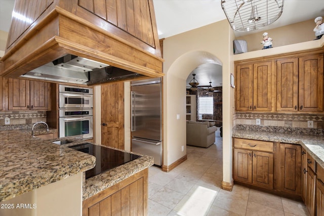 kitchen with stone countertops, stainless steel appliances, a sink, backsplash, and brown cabinetry