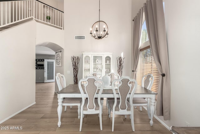 dining space featuring visible vents, arched walkways, a towering ceiling, wood finished floors, and a chandelier