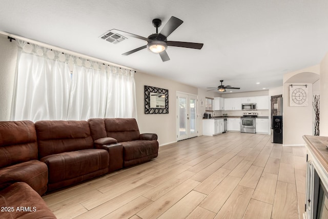 living room featuring arched walkways, visible vents, light wood-style floors, a ceiling fan, and baseboards