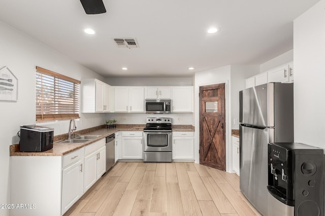 kitchen with visible vents, white cabinets, light wood-style flooring, stainless steel appliances, and a sink