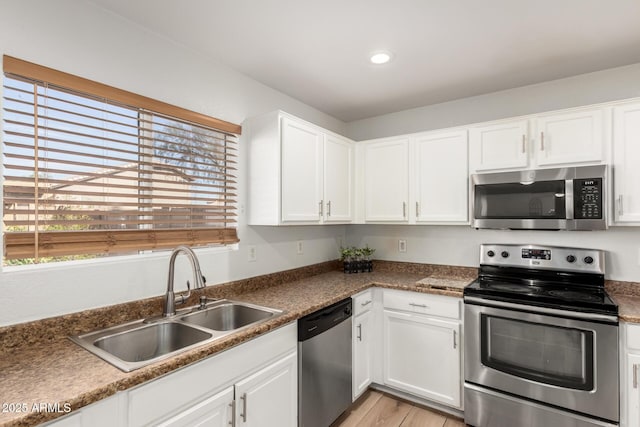 kitchen with stainless steel appliances, a sink, a wealth of natural light, and white cabinetry