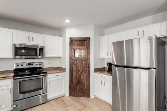 kitchen featuring wood tiled floor, appliances with stainless steel finishes, white cabinets, and dark stone countertops