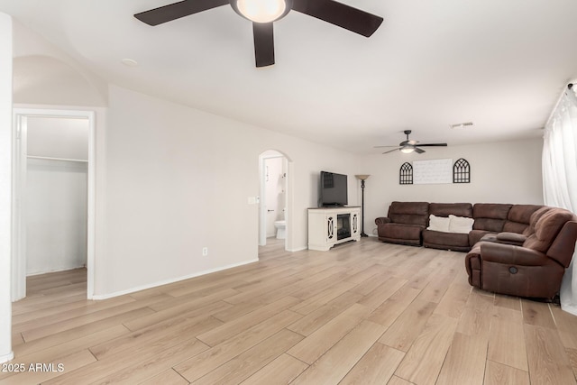 living room with arched walkways, ceiling fan, visible vents, baseboards, and light wood-style floors