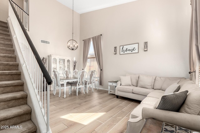 living room featuring visible vents, stairway, a high ceiling, an inviting chandelier, and light wood-style floors