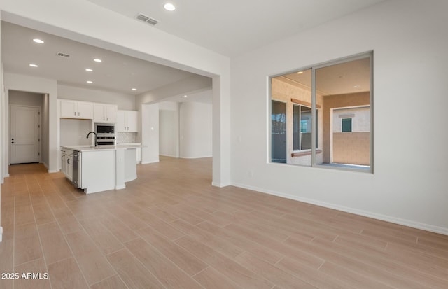 kitchen featuring light countertops, visible vents, open floor plan, white cabinets, and a kitchen island with sink