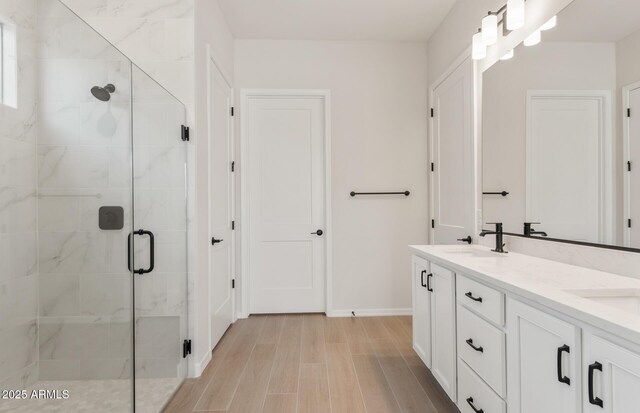 full bathroom featuring double vanity, baseboards, wood finished floors, a shower stall, and a sink