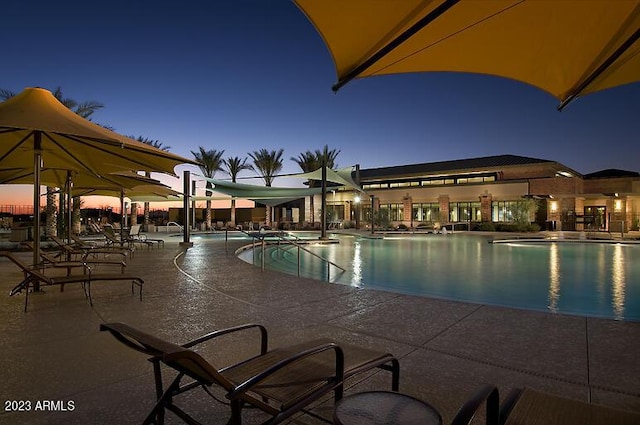 pool at dusk featuring a patio area and a community pool