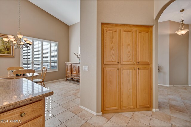 kitchen featuring light tile patterned flooring, light stone counters, light brown cabinets, pendant lighting, and a notable chandelier