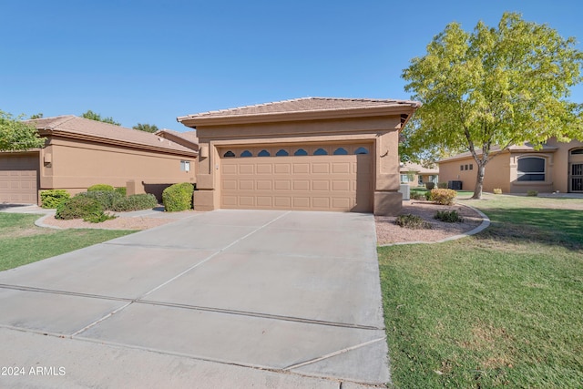 view of front facade with stucco siding, a tiled roof, driveway, a front yard, and a garage