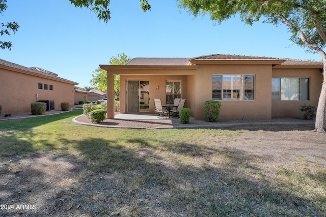 rear view of house featuring stucco siding, cooling unit, a lawn, and a patio area