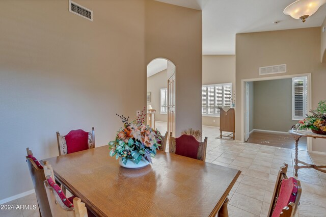 dining area featuring arched walkways, a high ceiling, visible vents, and light tile patterned floors
