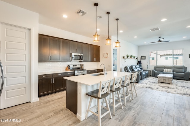 kitchen featuring a breakfast bar area, pendant lighting, stainless steel appliances, a kitchen island with sink, and sink