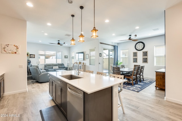 kitchen with pendant lighting, light hardwood / wood-style floors, a kitchen island with sink, and sink