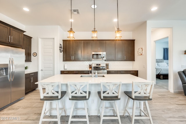 kitchen with stainless steel appliances, dark brown cabinetry, light wood-type flooring, and decorative light fixtures