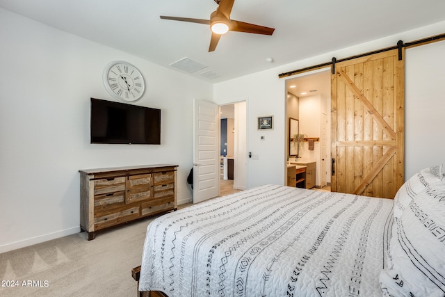 bedroom featuring a barn door, connected bathroom, ceiling fan, and light carpet