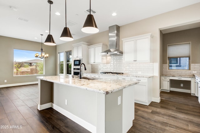 kitchen with wall chimney exhaust hood, sink, pendant lighting, a kitchen island with sink, and white cabinets