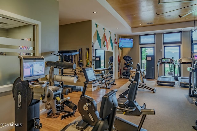 workout area with light wood-type flooring and a tray ceiling