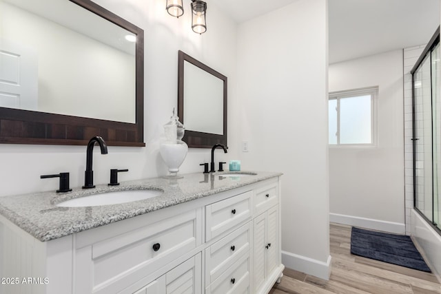 675 Val Verde Cir W, Litchfield Park, AZ 85340 - bathroom with double vanity, wood finished floors, baseboards, and bath / shower combo with glass door