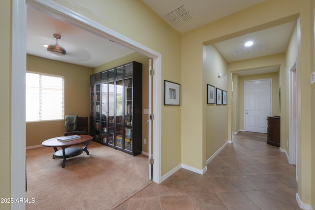 hall with carpet floors, baseboards, visible vents, and tile patterned flooring